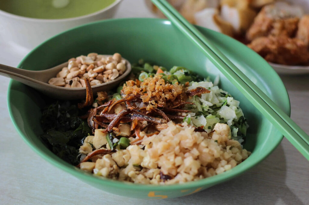 A bowl of thunder tea rice with chopsticks and a spoon resting beside it.