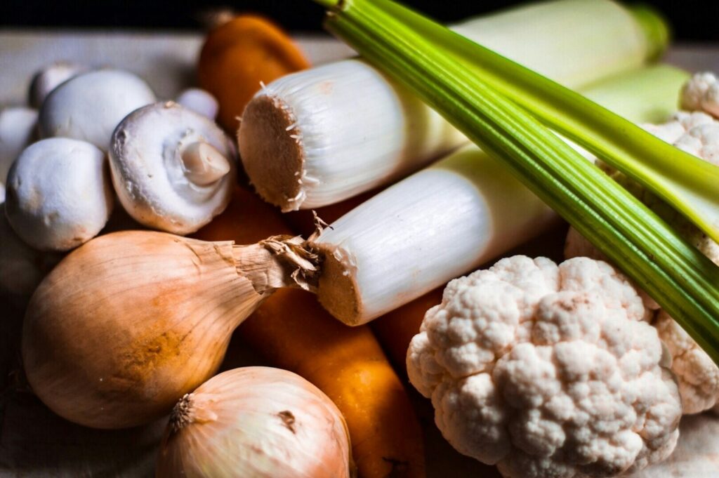 A colorful assortment of healthy vegetables: onions, celery, leeks, and carrots arranged together on a wooden surface.