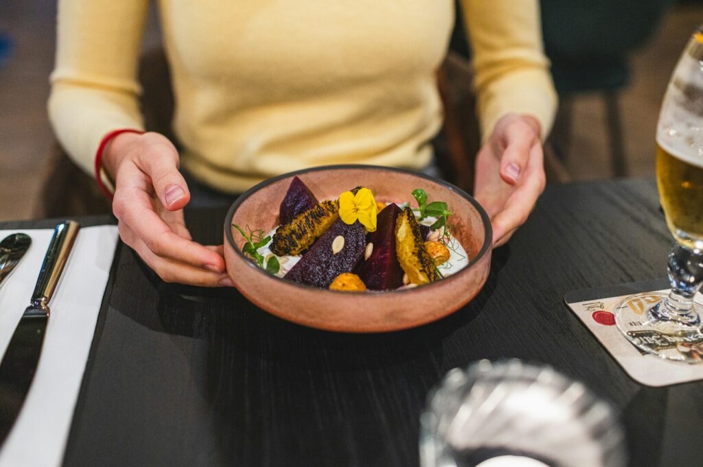 A woman proudly displays a bowl of nutritious food from a restaurant, showcasing her healthy meal choice.
