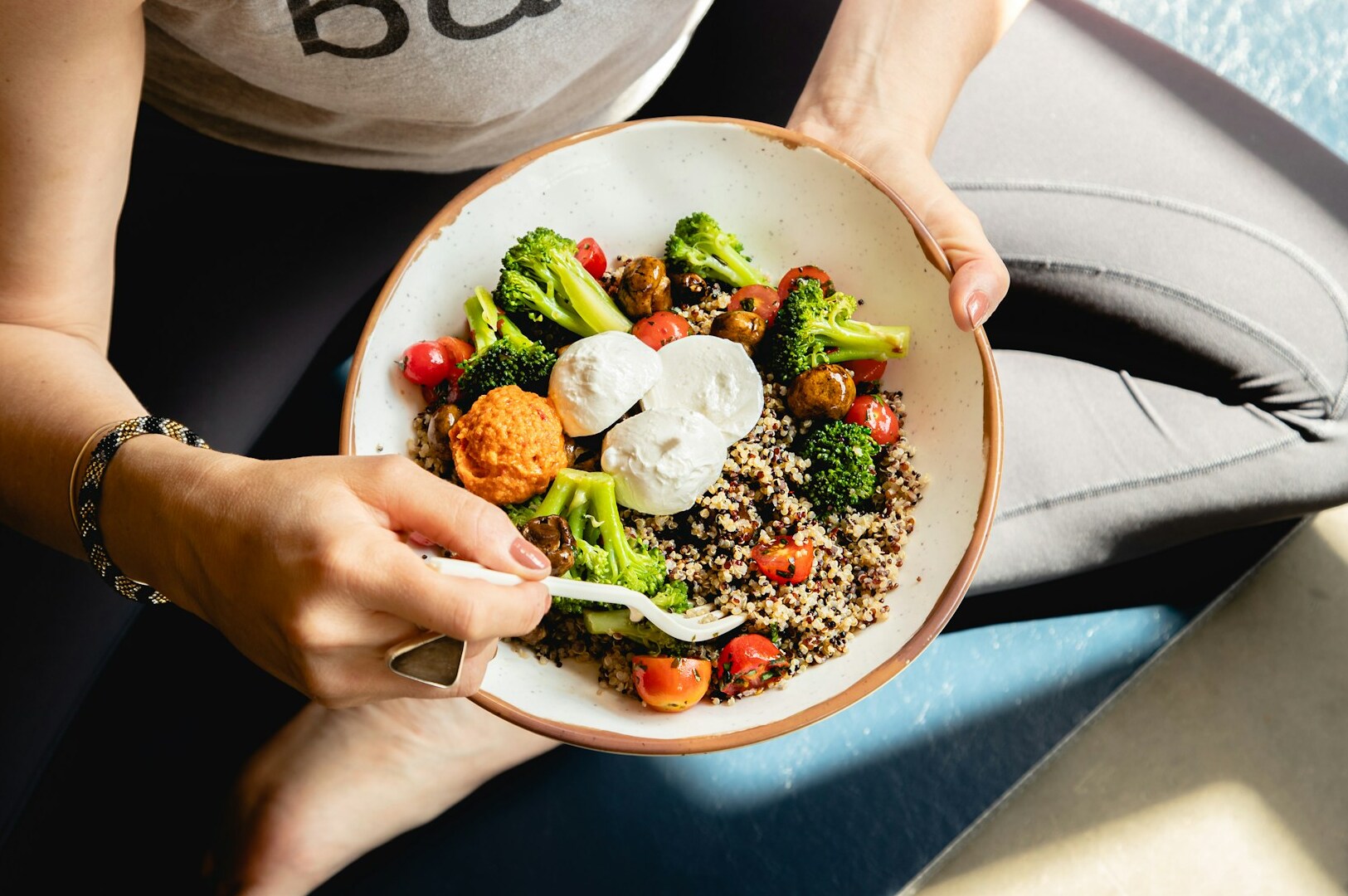 A person holds a fork above a bowl of healthy food at a restaurant, ready to take a bite.