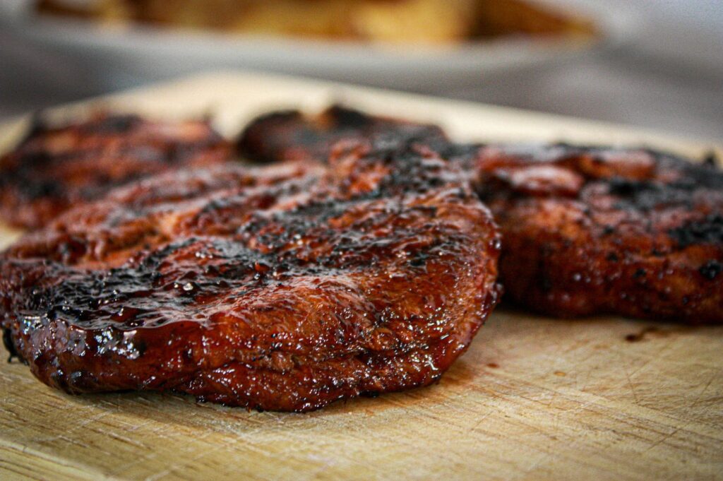 A charred lion’s mane steak resting on a wooden cutting board, showcasing its rich texture and color.