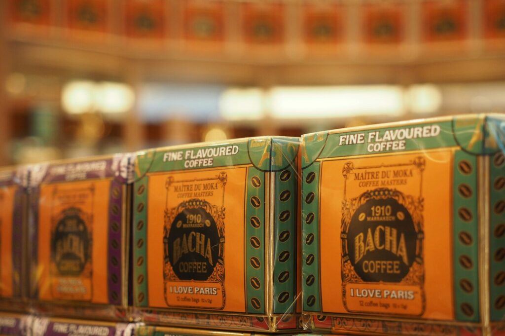 Close-up of colorful Bacha Coffee packages with "Fine Flavoured Coffee" label. Warm lighting creates an inviting ambiance, highlighting premium branding.