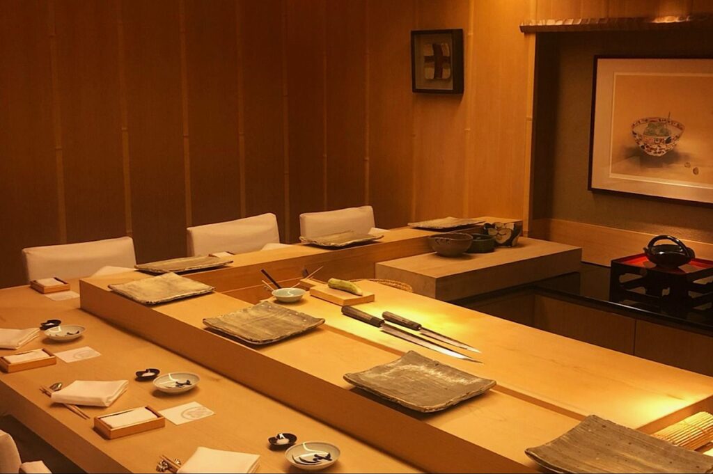 Elegant sushi bar with a warm, wooden interior. Plates and utensils are neatly arranged on the counter, conveying a serene and inviting atmosphere.