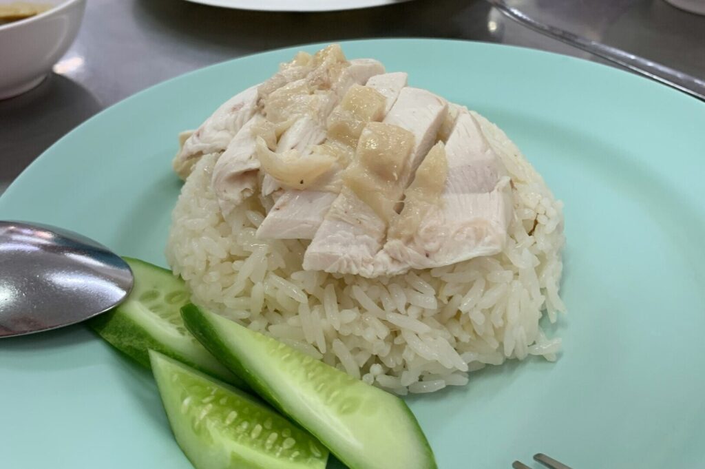 A serving of chicken rice on a plate, showcasing succulent chicken pieces atop a mound of rice.