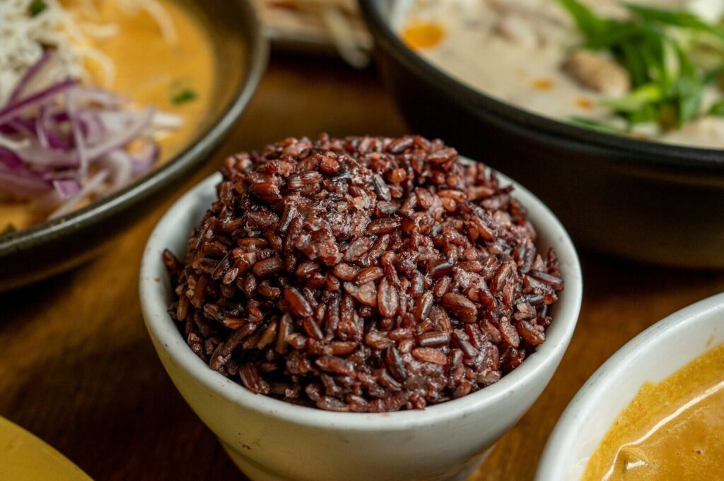 A bowl of brown rice next to a steaming bowl of soup, highlighting a comforting dining experience.