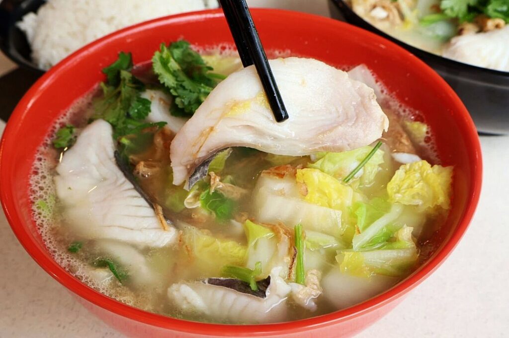 A bowl of sliced fish soup filled with fresh vegetables and tender fish pieces, garnished for presentation.