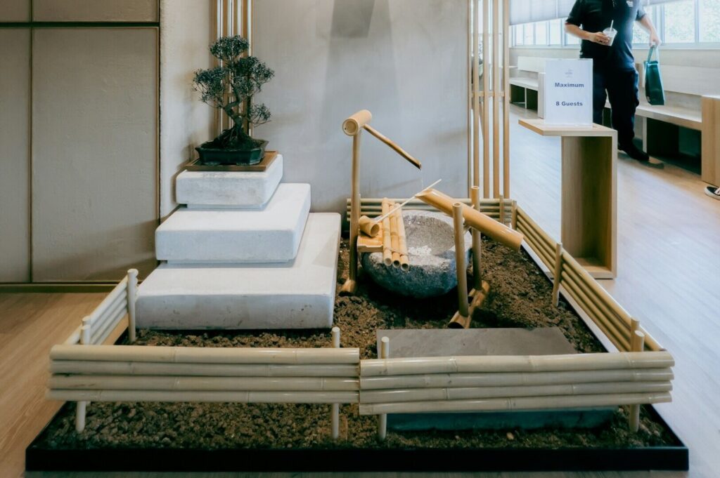 A miniature Zen garden in a room with bamboo elements, small stone steps, a bonsai tree, and a water feature, conveying tranquility and balance.