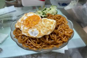A serving of Singapore Noodles garnished with a sunny-side-up egg, highlighting a delicious Asian-inspired meal.