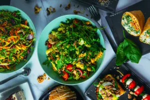 Aerial view of a colorful spread featuring a pasta salad with arugula, tomato, and olives, wraps, bruschetta, cake, and capprese. Fresh and inviting.