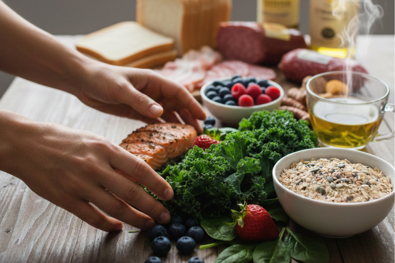 A person preparing a meal with nutrient-dense ingredients, including salmon, kale, berries, grains, and tea.