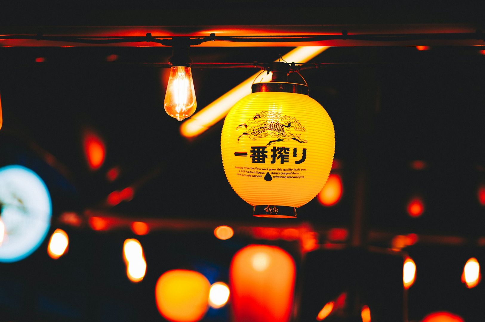 A glowing yellow paper lantern with Japanese characters is surrounded by warm lights, creating a festive and inviting ambiance against a dark background.