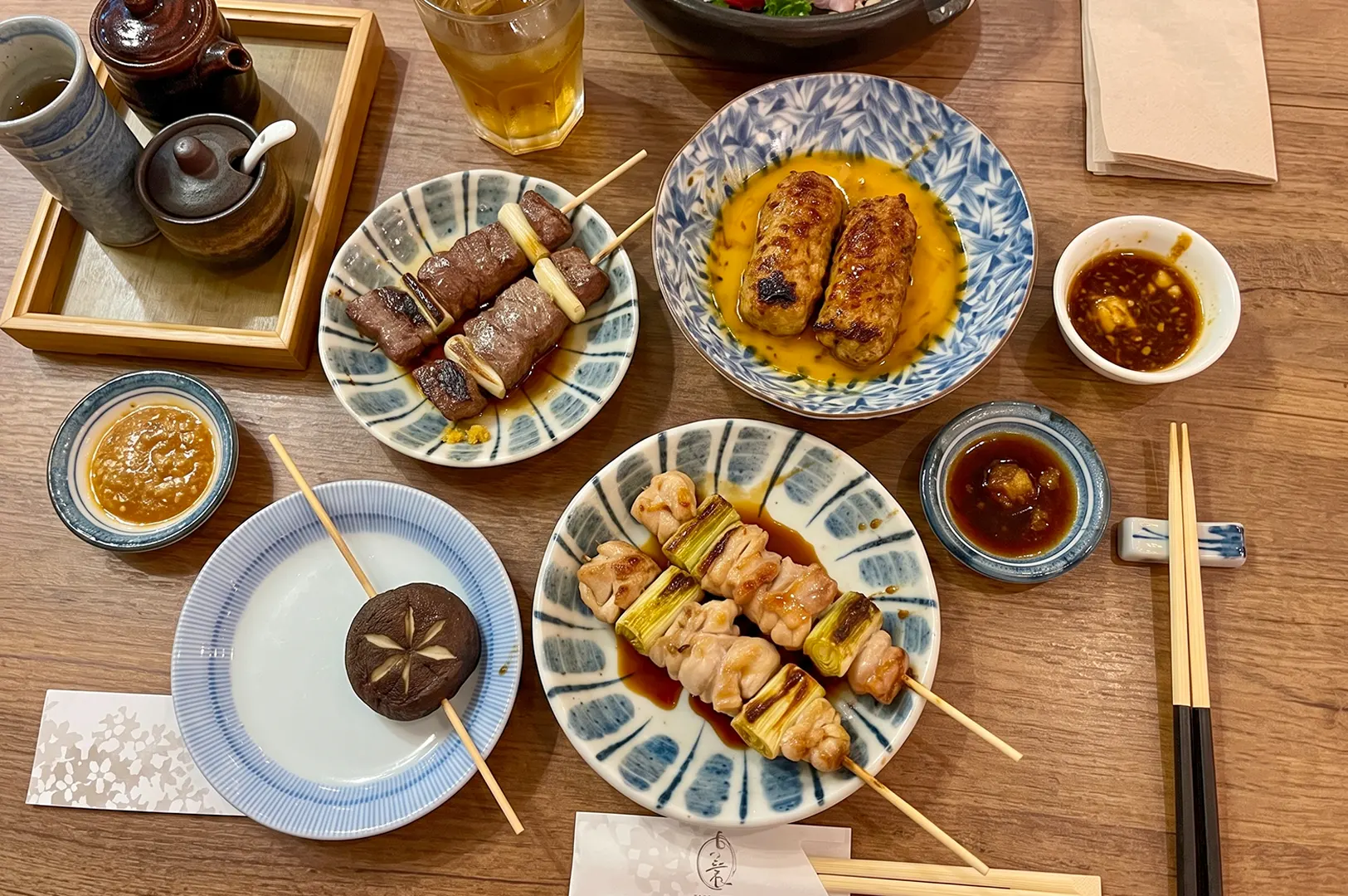 Assorted Japanese izakaya dishes featuring grilled chicken yakitori skewers, tsukune, and dipping sauces.