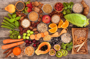 Assorted healthy foods on a wooden table, including fruits, vegetables, grains, and spices. The colorful arrangement conveys freshness and variety.