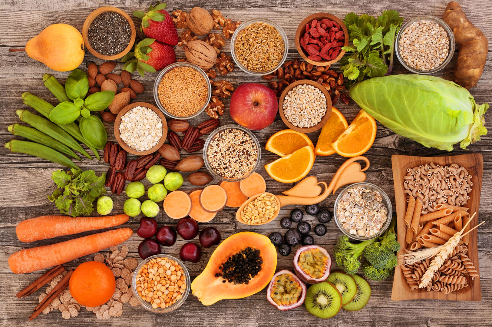 Assorted healthy foods on a wooden table, including fruits, vegetables, grains, and spices. The colorful arrangement conveys freshness and variety.