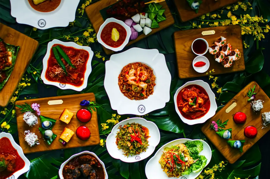 An array of colorful Indonesian dishes on wooden boards and white plates, garnished with vegetables and sauces, set against lush green leaves.