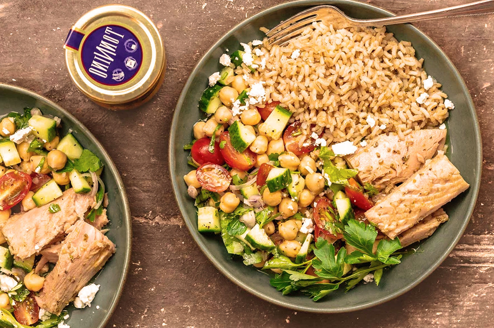 A plate with brown rice, tuna, a chickpea salad with cucumbers and tomatoes, and a jar of condiment in the background.