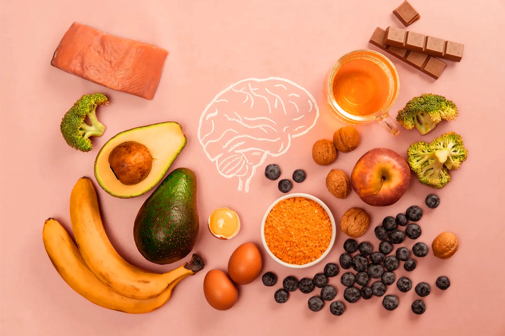 Various healthy foods, including salmon, avocado, bananas, broccoli, eggs, honey, nuts, blueberries, and chocolate, are arranged around a chalk-drawn brain on a pink background.