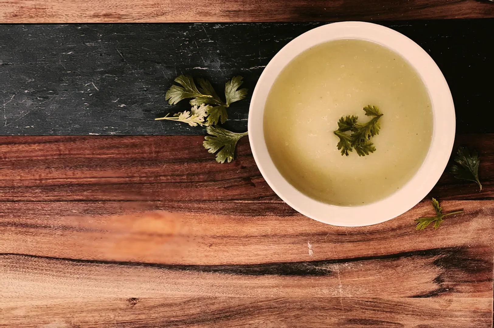 A bowl of creamy green soup garnished with fresh parsley on a rustic wooden table. The setting conveys warmth and a homemade feel.