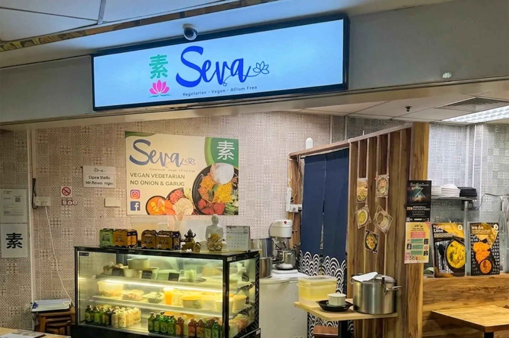 Seva Vegan Vegetarian restaurant storefront with a glass display case and menu signs.