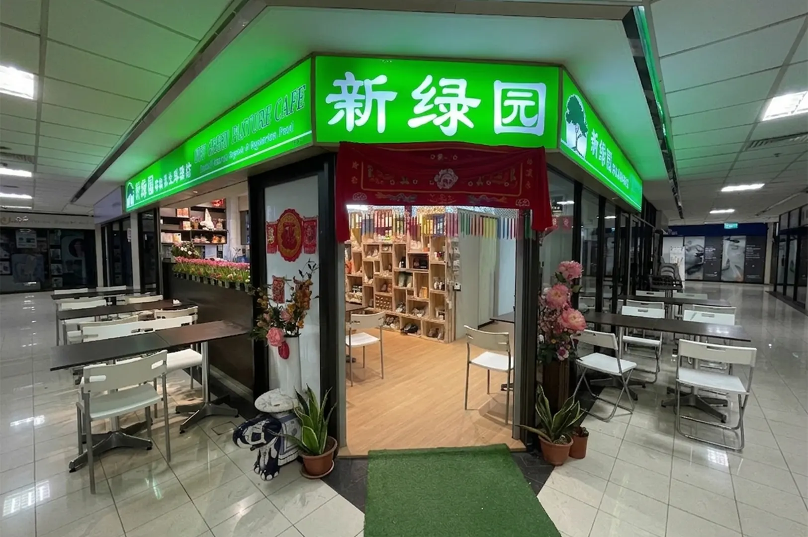 Storefront of Xin Lu Yuan featuring a bright neon green overhead signboard, a glass entrance, and shelves filled with products visible inside.