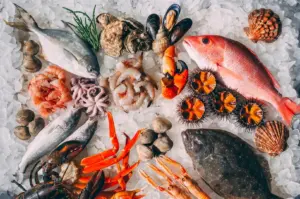 Fresh seafood assortment including whole fish, lobster, shrimp, and shellfish on a bed of ice.