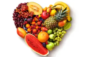 A heart-shaped arrangement of colorful fruits, including pineapple, watermelon, grapes, and bananas, on a white background, conveying a vibrant, healthy theme.