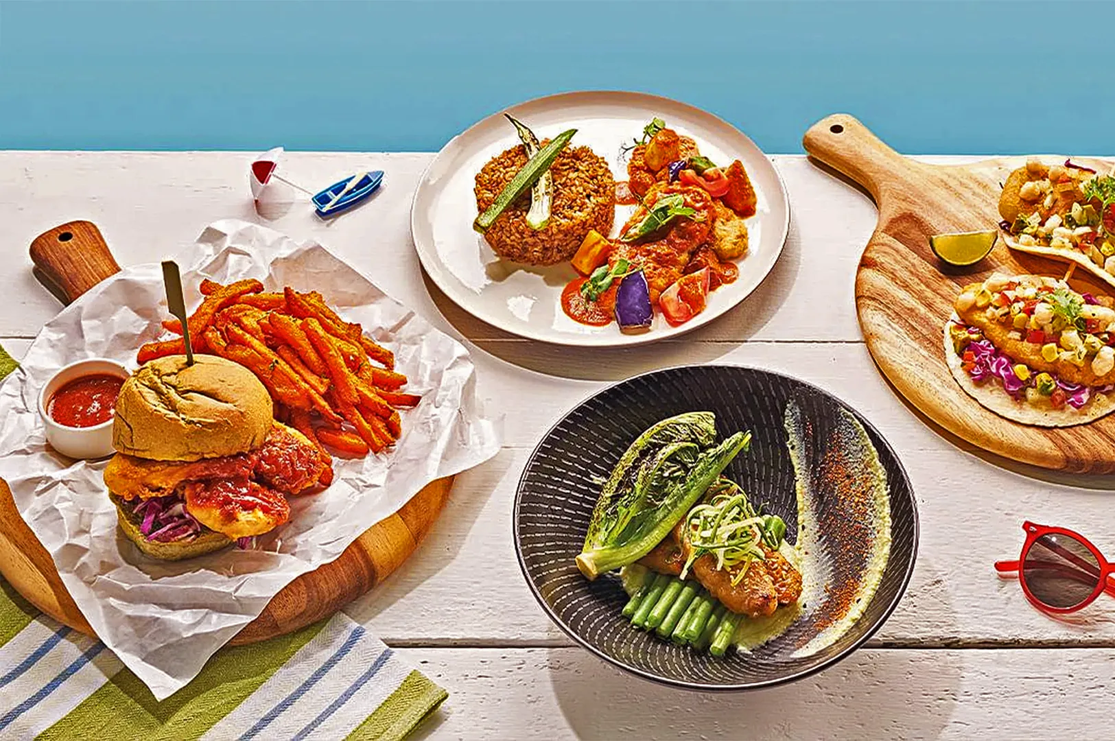 A vibrant layout of gourmet dishes: a burger with sweet potato fries, a plate of rice and vegetables, tacos, and a bowl of grilled fish with asparagus.