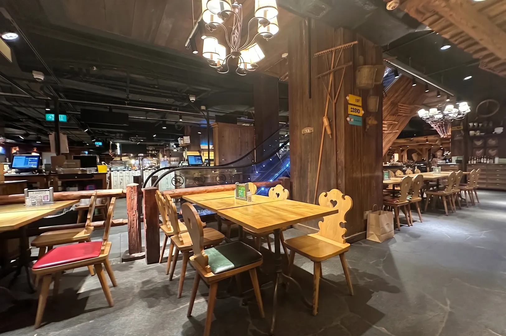 Rustic dining area inside Marché Mövenpick restaurant featuring Swiss chalet decor, wooden tables, and an escalator.