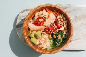 Fresh shrimp poke bowl with avocado, seaweed salad, carrots, and peanuts in a wooden bowl.