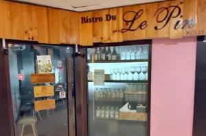 The storefront of Bistro Du Le Pin features a wooden facade, glass doors, and a display of wine bottles and glassware inside.