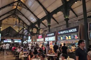 Crowded indoor food court at Lau Pa Sat market in Singapore with Victorian-style iron architecture and various dessert and juice stalls.