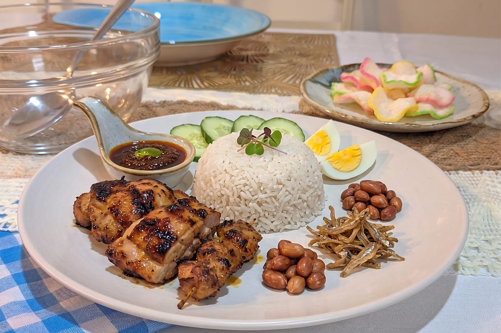 Traditional Nasi Lemak plate with grilled chicken, satay, sambal, peanuts, anchovies, and hard-boiled egg.
