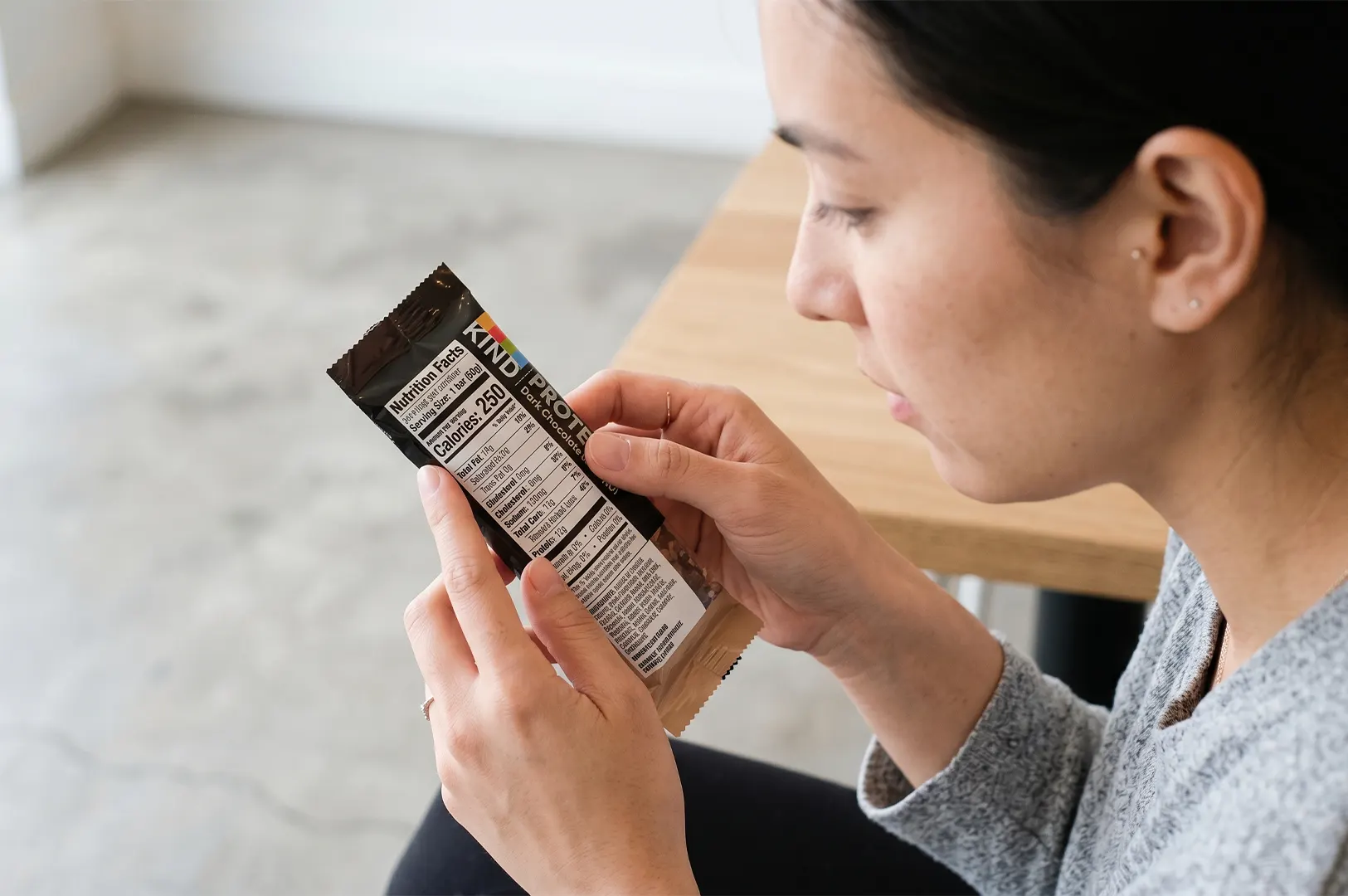 A woman reading the nutrition facts label on the back of a KIND Protein Dark Chocolate Nut bar.