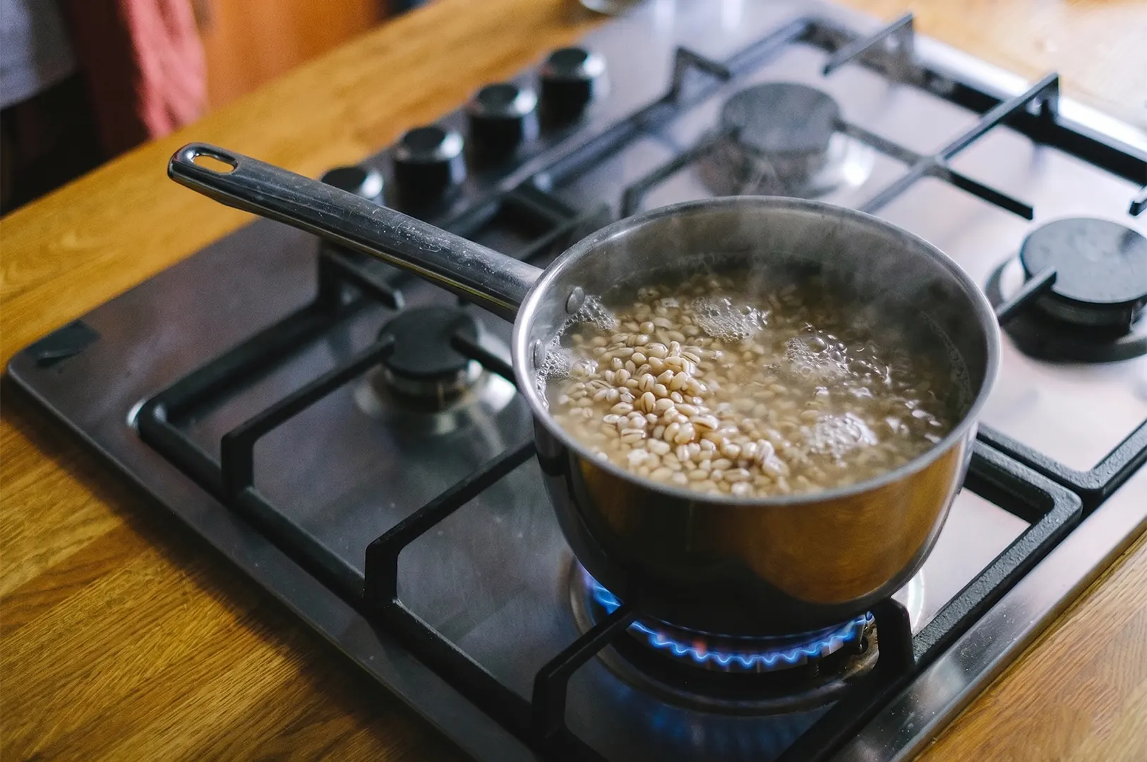 Boiling barley grains in a stainless steel pot on a gas stove.