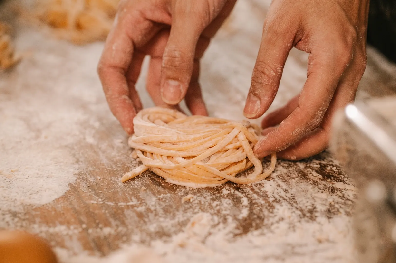 Close-up of hands preparing a nest of fresh handmade ramen noodles on a floured wooden surface.