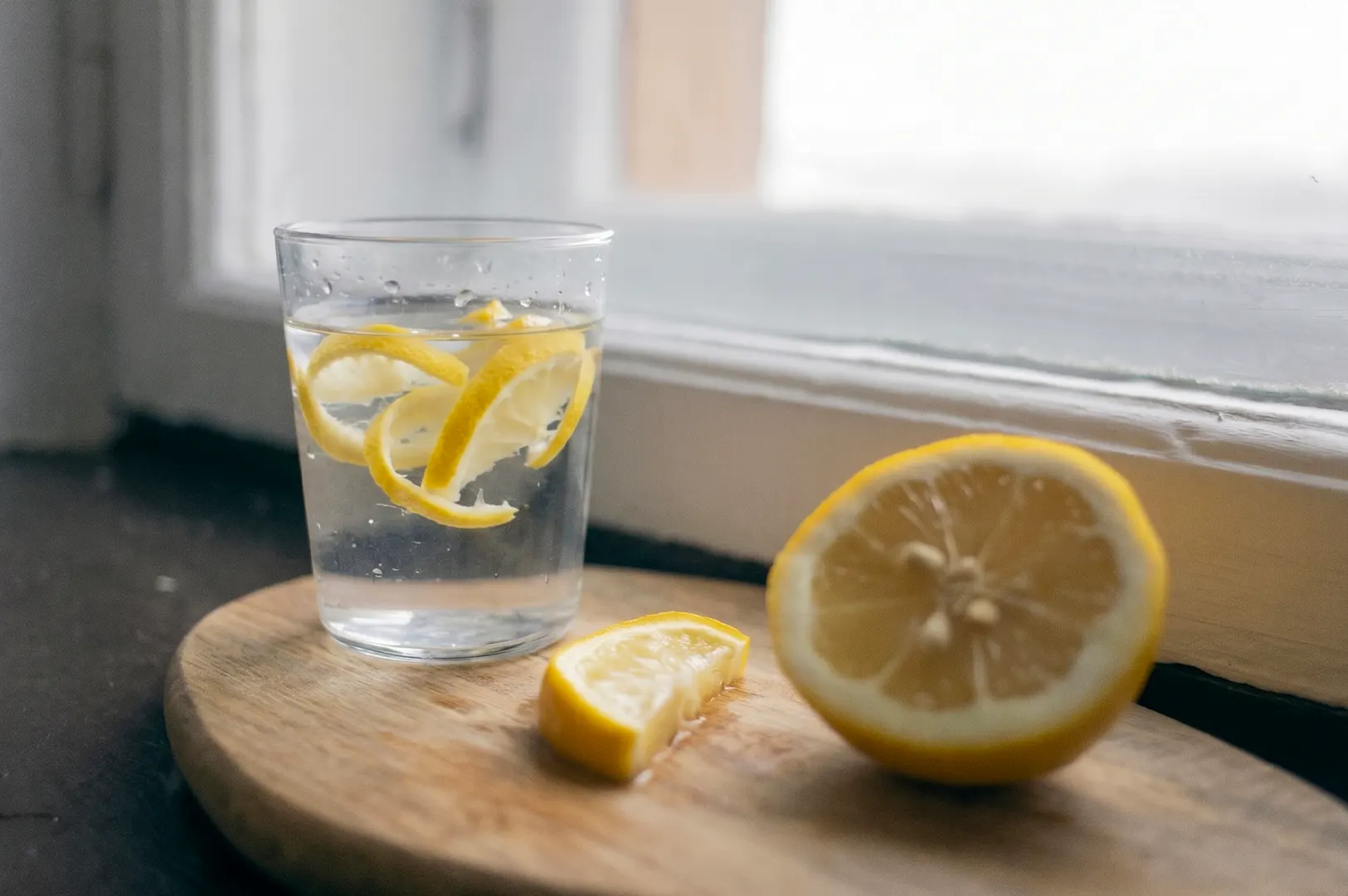A glass of fresh lemon water next to sliced lemons on a wooden cutting board.