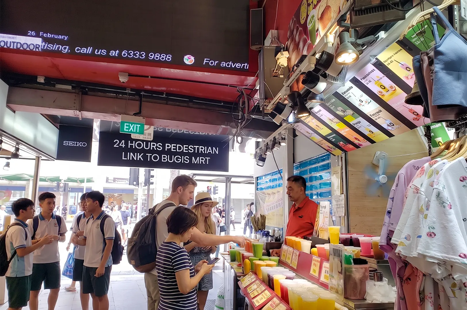 Customers ordering fresh juice at an outdoor street stall near the Bugis MRT pedestrian linkway in Singapore.