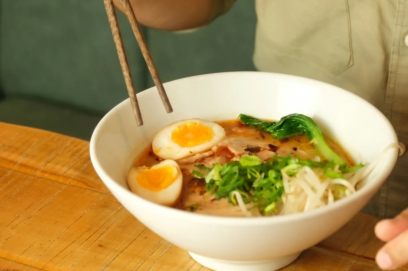 A bowl of miso ramen with soft-boiled eggs, scallions, bean sprouts, and bok choy, served with wooden chopsticks.