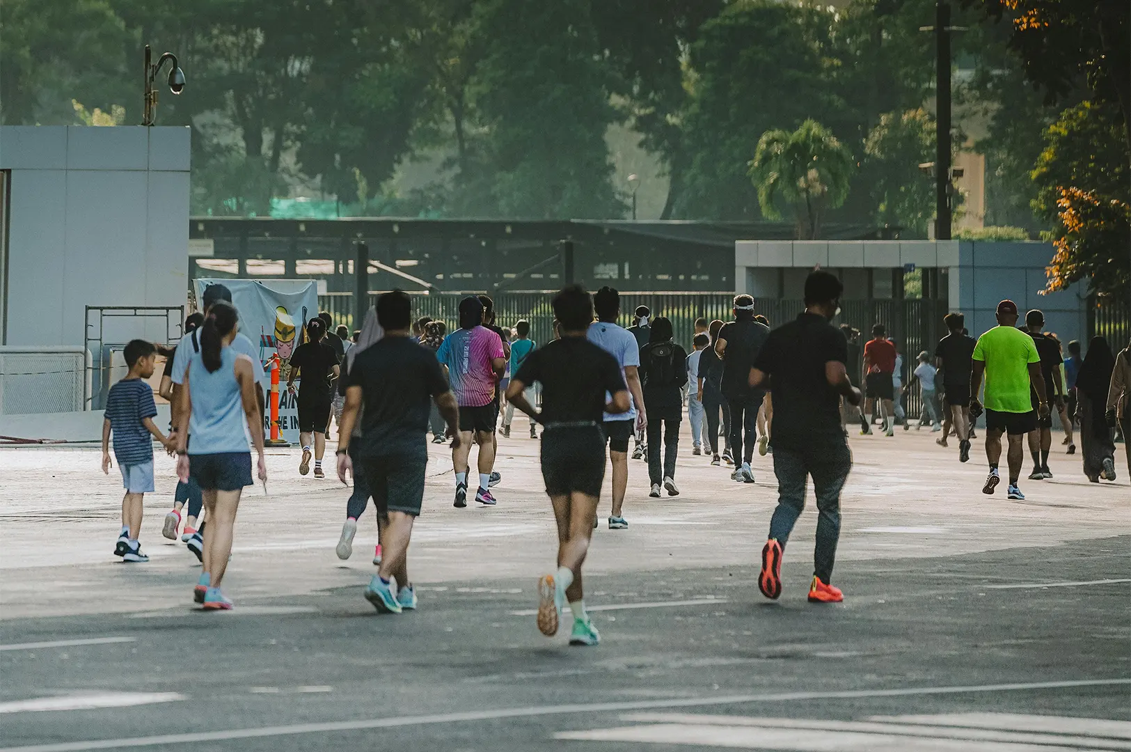 A large group of people running and walking on a wide paved path in an outdoor park during the day.