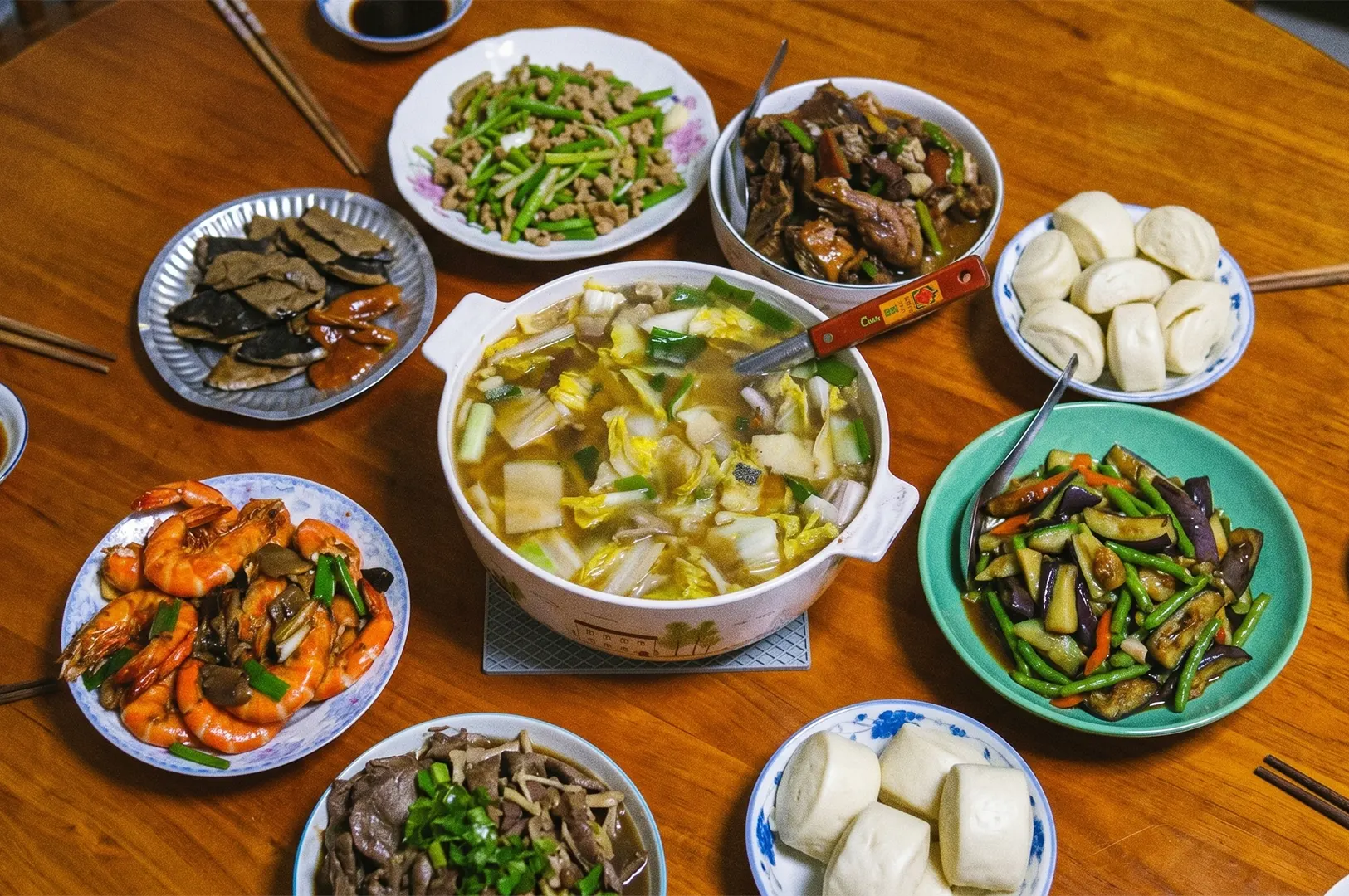 Traditional Chinese family dinner spread featuring Napa cabbage soup, stir-fried shrimp, braised eggplant with green beans, and steamed mantou buns.