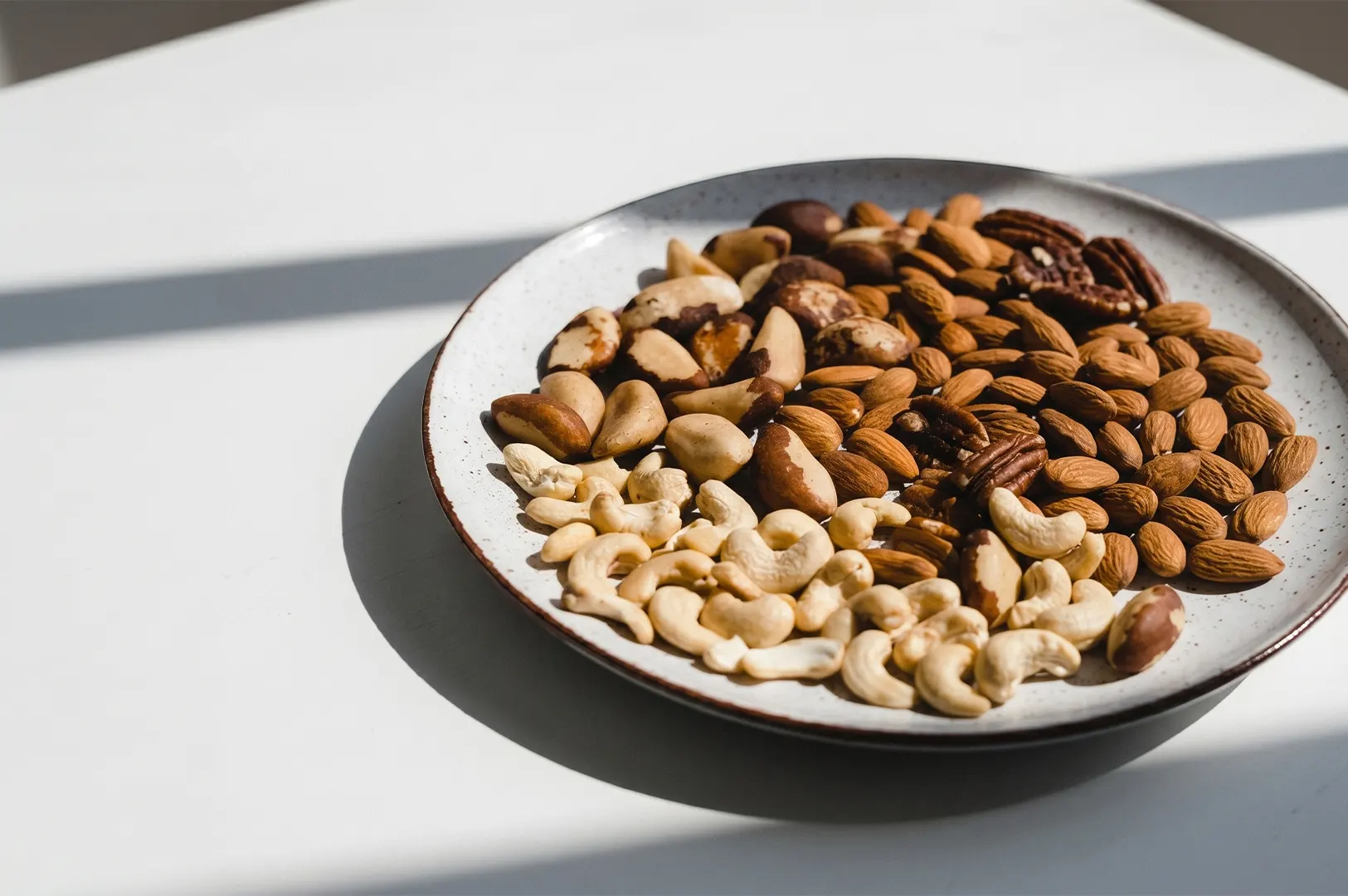 Mixed nuts platter featuring almonds, cashews, pecans, and Brazil nuts served on a ceramic plate.