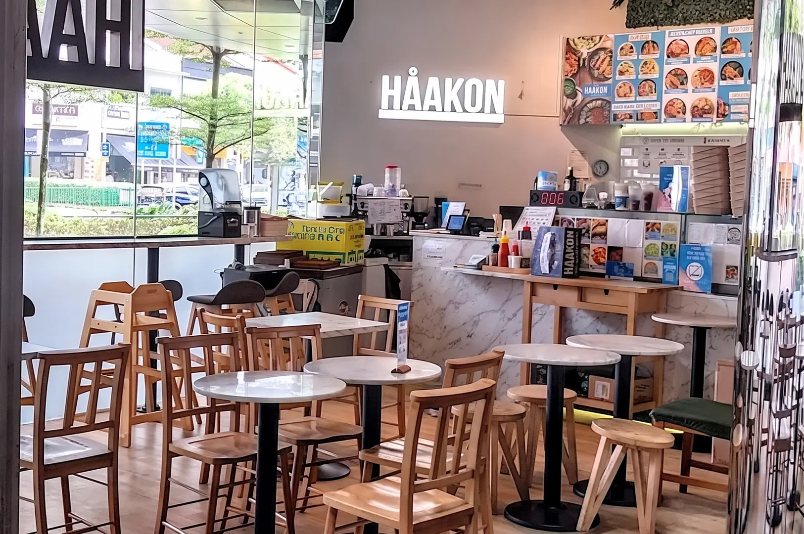 The interior of Håakon restaurant featuring wooden tables and chairs, a marble-topped service counter, and a menu board.