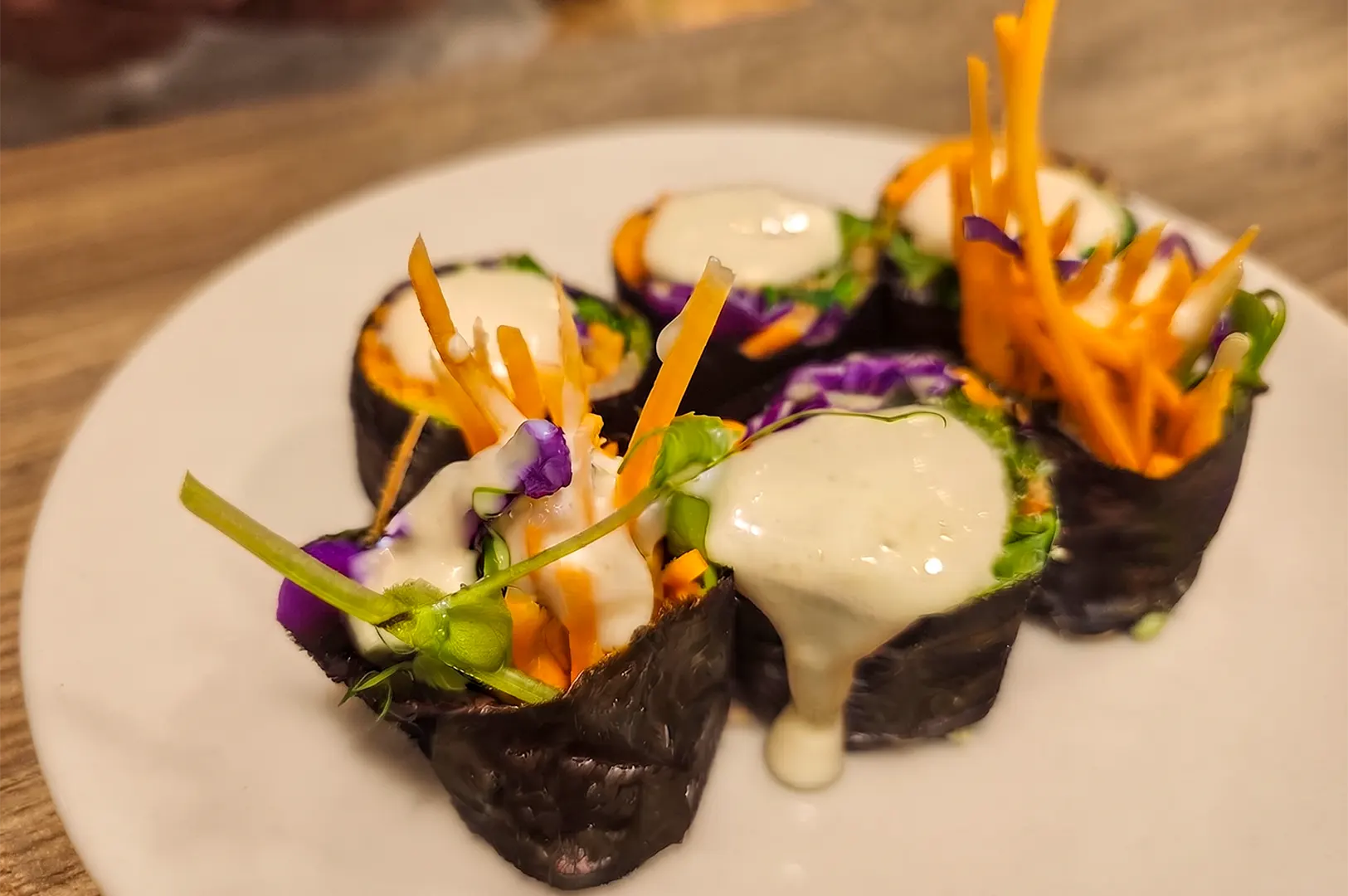 Fresh seaweed rolls filled with vegetables and drizzled with creamy sauce on a white plate.
