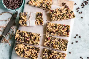 Homemade quinoa granola bars with pumpkin seeds and chocolate chips on a wooden board.