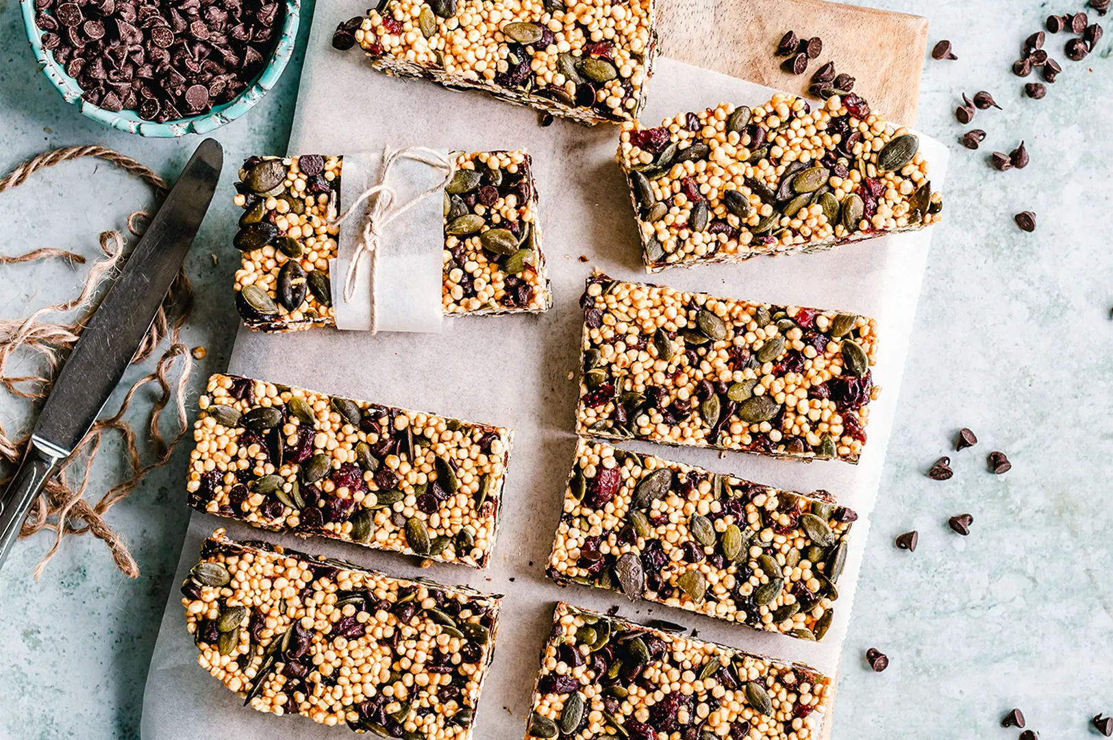 Homemade quinoa granola bars with pumpkin seeds and chocolate chips on a wooden board.