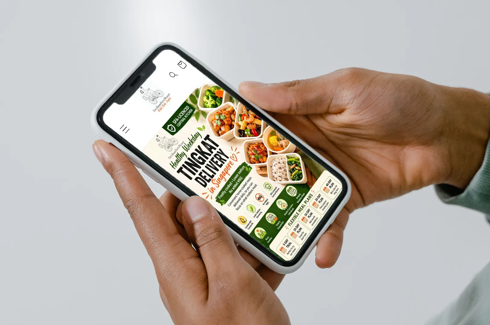 Person holding a smartphone displaying the healthy Tingkat meal delivery service website in Singapore.
