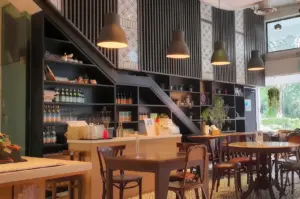Interior of The Living Cafe featuring a modern wooden counter, dark shelving, pendant lighting, and bistro-style seating.