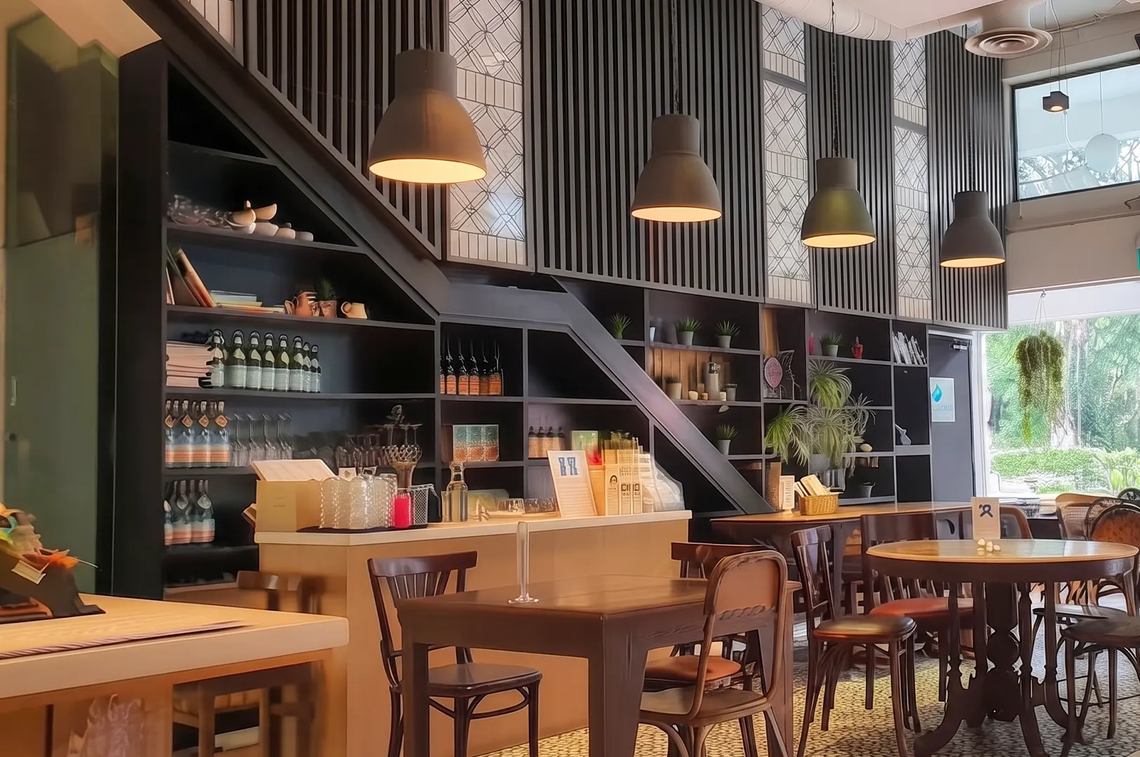 Interior of The Living Cafe featuring a modern wooden counter, dark shelving, pendant lighting, and bistro-style seating.