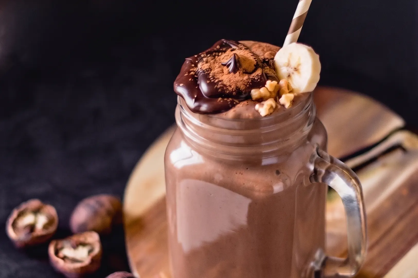 Chocolate monkey smoothie in a glass mason jar topped with chocolate sauce, walnuts, and a fresh banana slice.