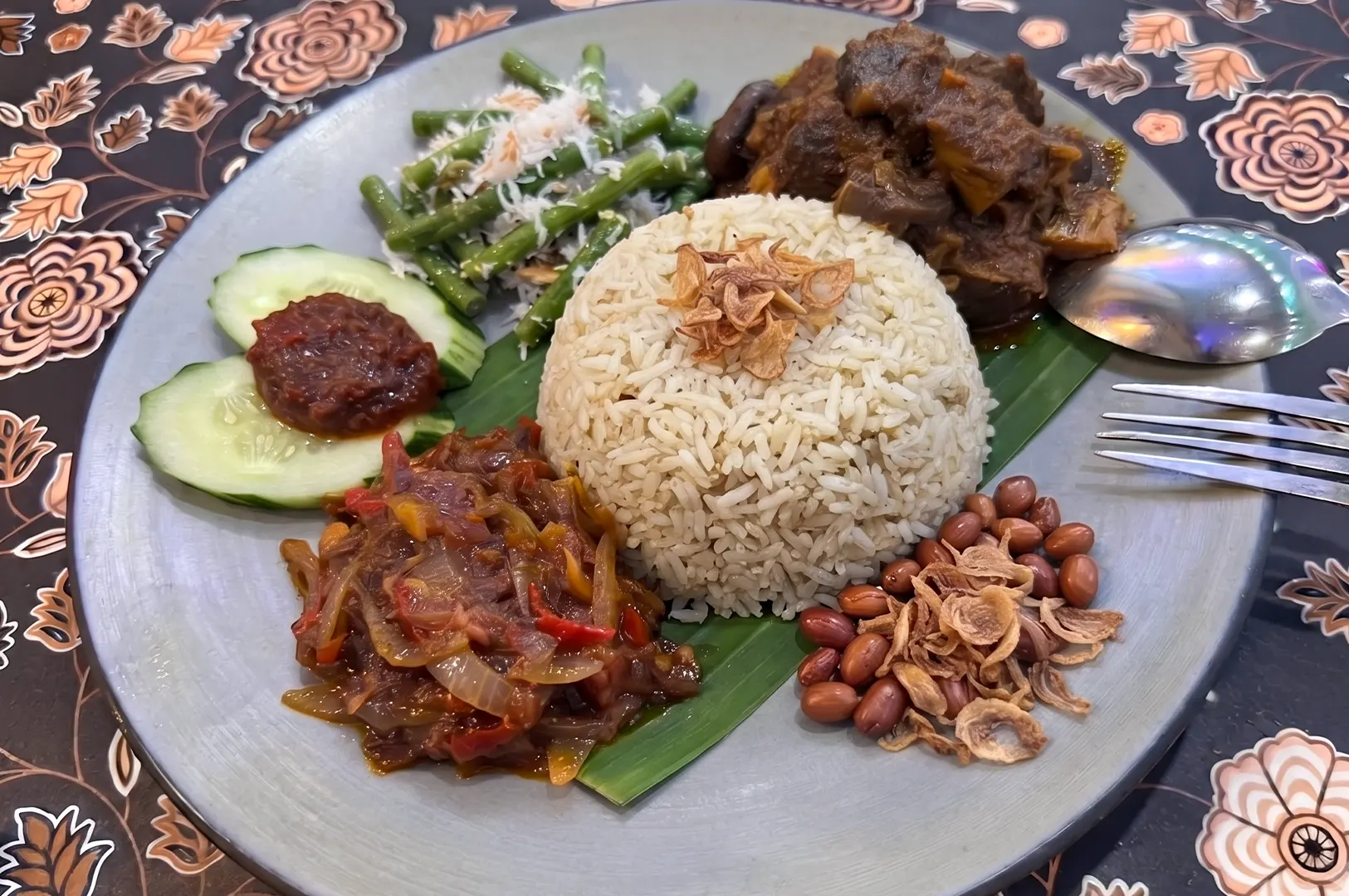 Vegan nasi lemak with plant-based beef rendang, sambal, cucumber, peanuts, and long beans on a plate.